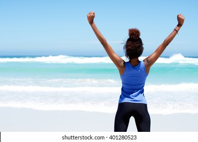 Rear view portrait of fitness woman stretching at beach with her hands raised