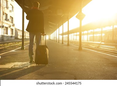 Rear view portrait of a man standing with bag and mobile phone at train station