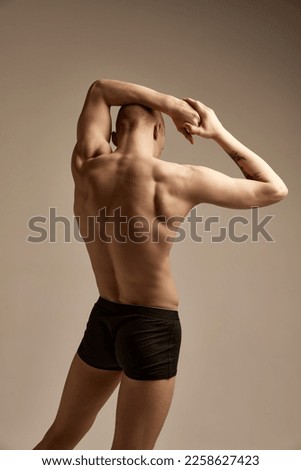 Rear view portrait of muscular male body, relief back over grey studio background. Young model posing in underwear. Concept of men's health and beauty, body and skin care, fitness. Body art