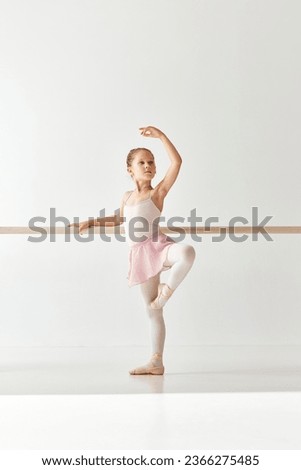 Rear view portrait of small adorable ballerina dancer girl in rose tutu ballet dress on pointe posing and performing dance elements in studio, dance school. Concept of beauty, fashion, hobby, action.