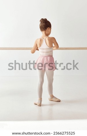 Rear view portrait of small adorable ballerina dancer girl in rose tutu ballet dress on pointe shoes classic variation practices ballet dancing. Education lessons. Concept of beauty, fashion, hobby.