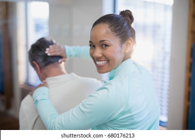 Rear view of portrait of smiling female therapist giving neck massaging to senior male patient at hospital ward