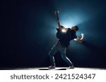 Rear view portrait of street style musician strumming chords on black guitar with dramatic on stage against black background with backlights. Concept of Rock-n-roll, music and dance, culture.