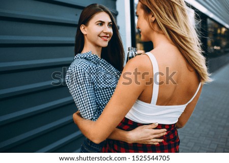 Rear view, portrait of two laughing girlfriends in summer clothes, spending their free time together walking around the city