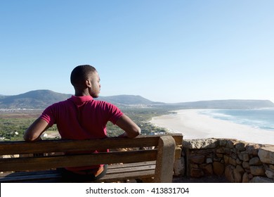 Rear view portrait of young african man sitting relaxed on a bench and looking at the sea, man on a holiday. - Powered by Shutterstock