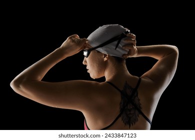 Rear view portrait of young woman, skilled swimmer adjusting swim cap and goggles against black studio background. Concept of professional sport, motion, strength and power, dynamic and energy. Ad - Powered by Shutterstock