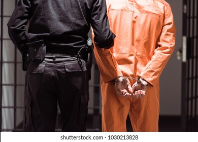 rear view of prison officer leading prisoner in handcuffs