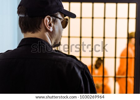 rear view of prison officer standing near prison cell with criminals