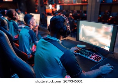Rear view of professional cybersport gamer playing video games and wearing headphones in dark interior of cybersport club
