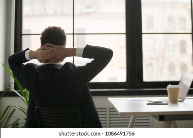 Rear view at relaxed businessman in suit enjoying break resting from work on laptop, man in suit holding hands behind head feeling no stress free relief relaxing or thinking planning future in office
