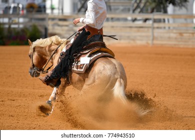 The rear view of a rider in cowboy chaps and boots sliding the horse into the sand