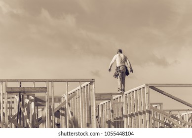 Rear View Roofer Builder On Wooden Roof Trusses Construction. Worker With Carpenter Tool Belt Working Balancing On Roofing. New Home Site House Foundation Framing In Irving, Texas, USA. Vintage