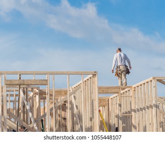 Rear View Roofer Builder On Wooden Roof Trusses Construction. Worker With Carpenter Tool Belt Working Balancing On Roofing. New Home Site House Foundation Framing In Irving, Texas, USA