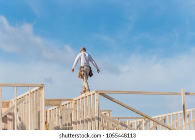 Rear View Roofer Builder On Wooden Roof Trusses Construction. Worker With Carpenter Tool Belt Working Balancing On Roofing. New Home Site House Foundation Framing In Irving, Texas, USA