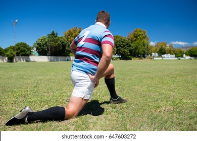 Rear view of rugby player exercising while kneeling on grassy field against sky - Powered by Shutterstock