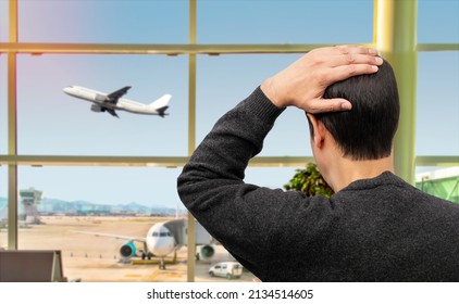 Rear view of a sad man looking at a plane taking off and missing his flight at airport.
