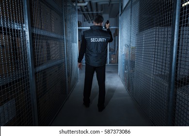 Rear View Of A Security Guard Standing In The Warehouse Holding Flashlight - Powered by Shutterstock