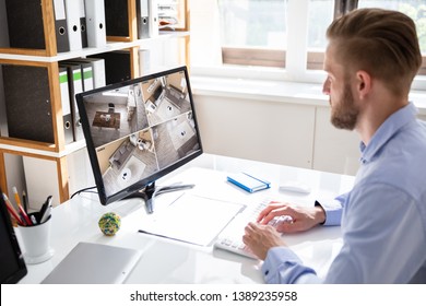 Rear View Of Security System Operator Looking At CCTV Footage At Desk In Office