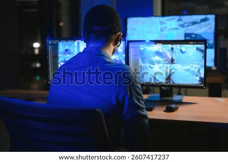 Rear view of security system operator looking at CCTV footage at desk in office.