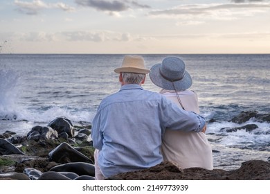 Rear view of senior caucasian couple sitting on the pebble beach hugging looking at horizon over water. Elderly relaxed couple enjoying nature and freedom in vacation or retirement - Powered by Shutterstock