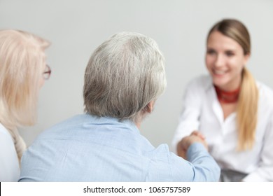 Rear View At Senior Couple Handshaking Medical Worker Visiting Doctor, Older Family And Financial Advisor Or Lawyer Shaking Hands At Meeting, Happy Grey-haired Aged Elderly Clients Making Deal