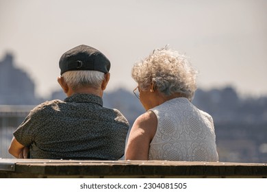 Rear view of a senior couple sitting on a wooden bench in the park. Elderly couple in the park on sunny day. Senior Retired couple sitting on the bench. Selective focus, copy space. - Powered by Shutterstock
