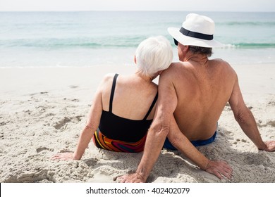 Rear View Of Senior Couple Sitting On Beach On A Sunny Day