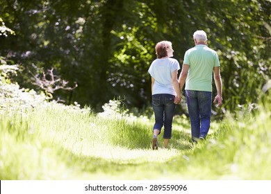 Rear View Of Senior Couple Walking In Summer Countryside