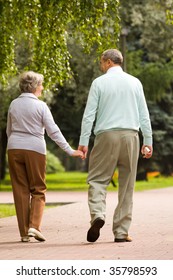 Rear View Of Senior Couple Walking Down In Park And Chatting