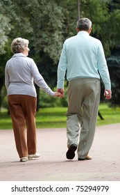 Rear View Of Senior Couple Walking Down In Park And Chatting