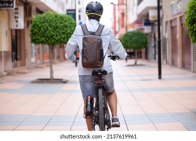 Rear View Of Senior Cyclist Woman Wearing Helmet On Electric Bicycle In City Street Looking Ahead. Active Elderly Grandmother Enjoying A Healthy Lifestyle And Freedom