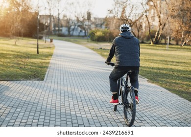 Rear view of a senior man is enjoying a peaceful bicycle ride through a serene city park at sunset. - Powered by Shutterstock