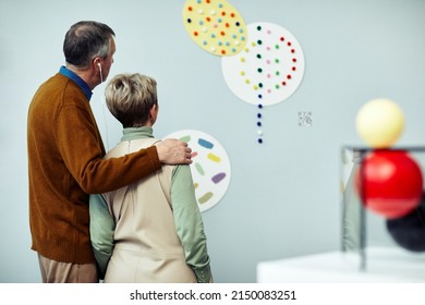 Rear View Of Senior Man And Woman In Love Having Audio Tour At Exhibition In Contemporary Art Museum