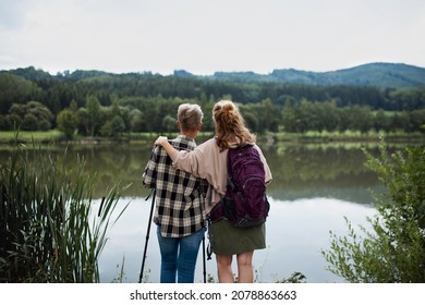 Rear View Of Senior Mother Embracing With Adult Daughter When Standing By Lake Outdoors In Nature