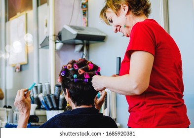 Rear View Of A Senior Woman At The Hair Salon. Happy Redhair Female Working As A Hairdresser And Cutting Hair Tips Of A Female Customer In A Beauty Center.Making New Hairstyle On Old Woman Short Hair