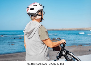 Rear view of senior woman with helmet looking at seascape enjoying a sunny day at the beach riding electric bicycle. Authentic retirement living and healthy lifestyle concept. - Powered by Shutterstock