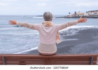 Rear View Of Senior Woman Sitting On A Bench Face To The Sea Looking At Horizon Over Water. Active Caucasian Elderly Woman  Enjoying Freedom And Vacation