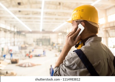 Rear View Of Serious Busy Construction Engineer In Yellow Hardhat Talking On Mobile Phone And Looking At Building Site While Solving Problems