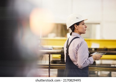 Rear View Of Serious Female Assembly Line Worker In Hardhat Standing At Conveyor And Controlling Movement Of Produced Details