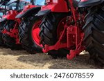 Rear view of several large modern red tractors standing in a field. Preparing for the start of the agricultural season.