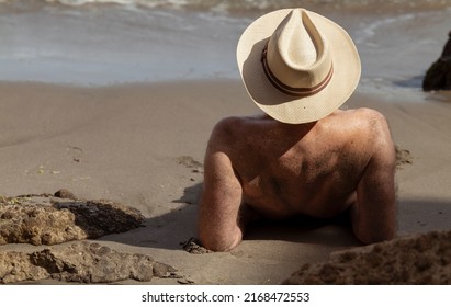 Rear View Of Shirtless Man In Hat Lying Down On Beach