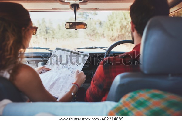 Rear view shot of couple driving on country road.\
Woman holding a route map with man driving the car. Couple on\
adventurous road trip.