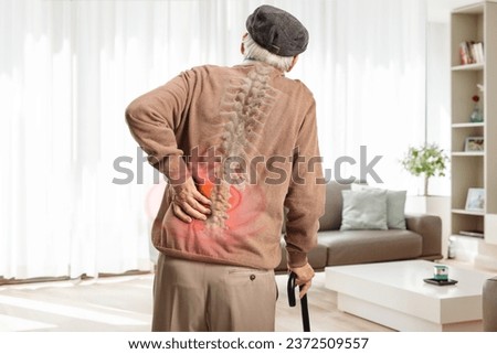 Rear view shot of an elderly man with a back pain and visible spine bone standing at home 