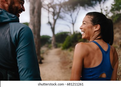 Rear view shot of fit couple smiling mountain trail. Young man and woman walking through country road in morning.
