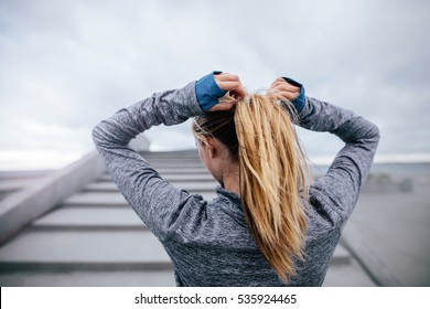 Rear view shot of fit female athlete tying hair before her workout. Young woman getting ready for training. - Powered by Shutterstock