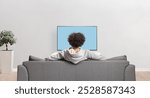 Rear view shot of a guy watching television and sitting on a sofa in an apartment