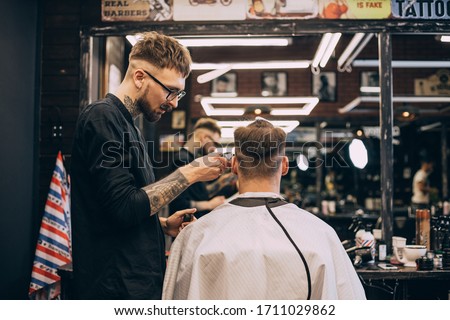 Rear view shot of handsome hairdresser cutting hair of male client. Hairstylist serving client at barber shop. Hipster young good looking man visiting hairstylist in barber shop.