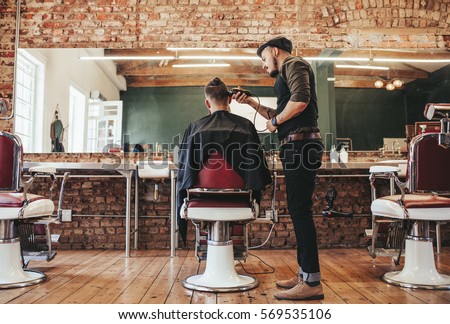 Rear view shot of handsome hairdresser cutting hair of male client. Hairstylist serving client at barber shop.