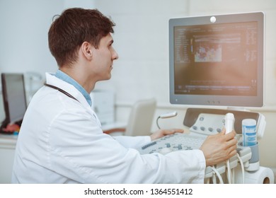 Rear view shot of a male doctor using ultrasound scanning machine at his clinic. Practitiner working on modern medical equipment at his office. Ultrasound diagnostics, pregnancy, cancer concept