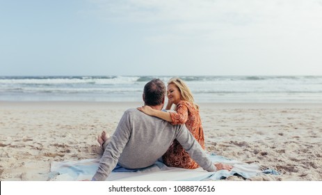 Rear view shot of mature man and woman sitting together on beach towel along the sea shore. Romantic senior couple relaxing on the beach. - Powered by Shutterstock